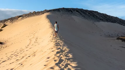 Cercles muraux Plage de Sotavento, Fuerteventura, Îles Canaries Joven de espaldas cruzando las dunas de arena blanca entre la luz del sol y la sombra junto a la playa de sotavento en Fuerteventura, islas canarias.