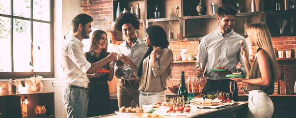 Group of cheerful young people enjoying home party with snacks and drinks