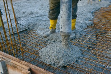 Bauarbeiter gießen die Bodenplatte eines Einfamilienhaus-Neubaus über der Baustahlmatte mit der...