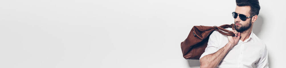 Handsome young man carrying bag on shoulder while standing against white background