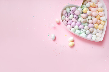 heart shaped box filled with easter eggs on a pastel pink background with confetti. top view. copy space. flat lay