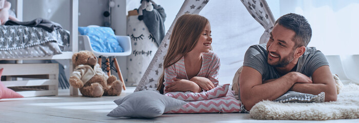 Happy father and his little daughter looking at each other while lying on the floor in bedroom © gstockstudio