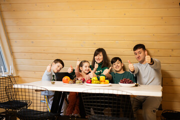 Family with three kids eat fruits in wooden country house on weekend and shows thumb up.