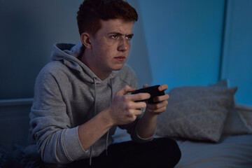 Caucasian teenage boy playing on game controller at night