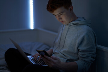 Focus caucasian teenage boy using laptop while sitting at night in his room