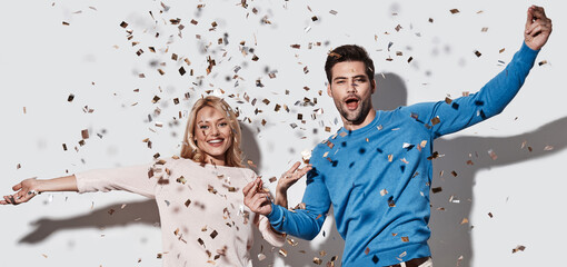Beautiful young couple throwing confetti and smiling while standing against grey background