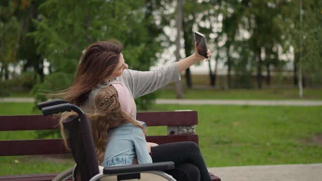 Woman enjoys making selfies with little girl in wheelchair
