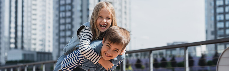 happy preteen boy in denim outfit piggybacking girl on urban street, banner. © LIGHTFIELD STUDIOS