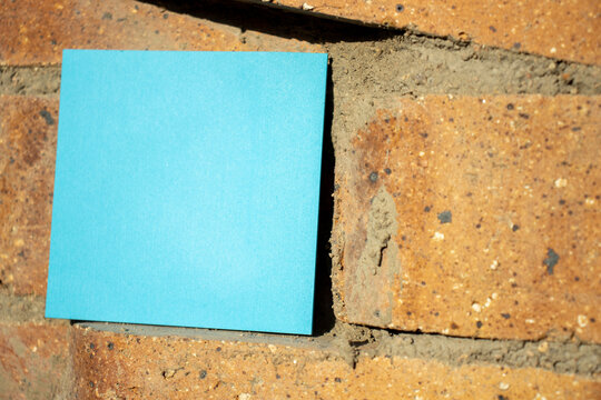 blue square paper note resting on a brick wall in full sun with empty free space for template or blank copy area