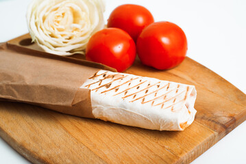 Cooked shawarma in pita bread on a wooden board with tomato ingredients, fast food