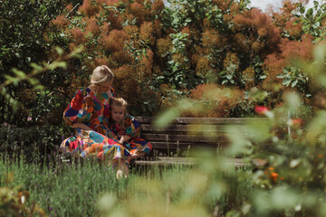 Mother and daughter are sitting on a bench in the park. Mom holds the girl by the hands. Image with selective focus, noise effects and toning. Focus on the girl and women.