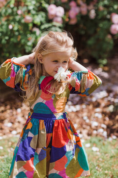 Summer spring portrait of pretty little girl wearing  dress, posing in rose garden smelling flowers. Happy smiling baby. Love of nature. spring mood