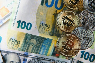 Close up heap of golden bitcoin physical coins on top of Euro, dollar banknotes background, high angle view, selective focus