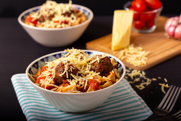 Classic italian tagliatelle spaghetti pasta with tomato sauce, meatballs, parmesan cheese and basil in plate on dark table. Dark food, dark mood