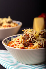 Classic italian tagliatelle spaghetti pasta with tomato sauce, meatballs, parmesan cheese and basil in plate on dark table. Dark food, dark mood