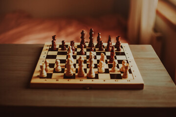 At home in a room on a gray table there is a chess board with beautiful elegant wooden figures....