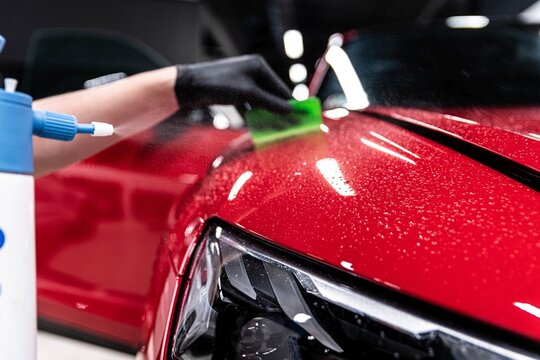 Application of a colorless protective film at a car detailing studio or car wash. Beautiful red car paint.