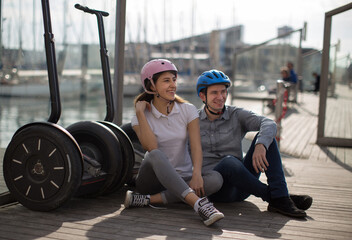 young couple guy and girl are walking on the segway along the board paved promenade in the port of...