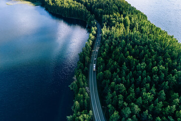 Aerial view of road in green woods and blue lakes water in Finland