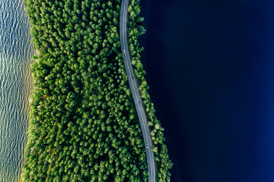 Aerial view of road in green woods and blue lakes water in Finland