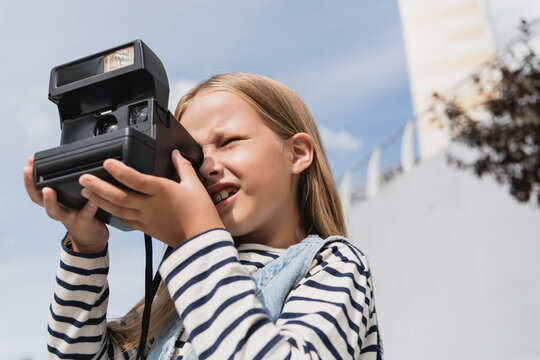 low angle view of girl in denim vest and striped long sleeve shirt taking photo of vintage camera.