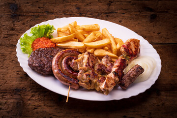 plate with mixed grill french fries on wooden table