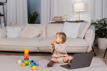 Side view of baby girl holding toy near laptop in living room.