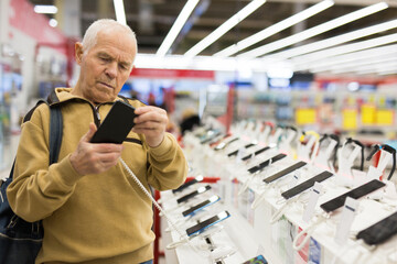 Fototapeta na wymiar elderly grayhaired man pensioner examining counter with electronic gadgets and tablets in showroom of digital goods store
