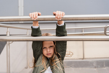 preteen girl in stylish bomber jacket leaning on metallic handrails near mall.