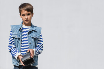 well dressed preteen boy in denim clothes holding vintage camera on grey background.