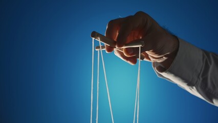 The hand of a man in a gray shirt controls a puppet using a wooden manipulator and strings on a...