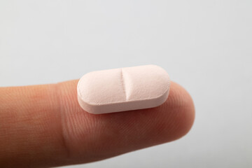 The pill on the finger extra close up. The white pill extra macro view.