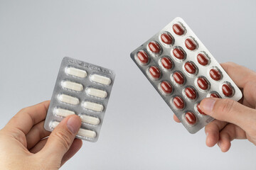 Hands holding a blister of pills on a grey background. Сomparison concept