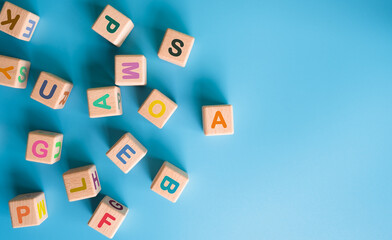 Colorful wooden cubes with letters scattered on blue background. learning, increasing IQ, development for children. Top view of children's toys. Educational games.
