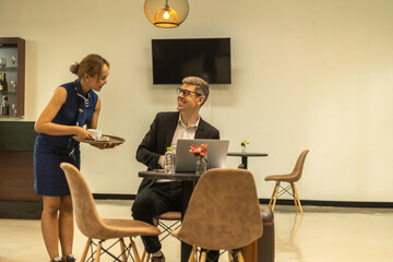 Business traveler enjoys having service from a female hostess in an exclusive airline lounge while...