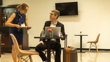 Business traveler enjoys having service from a female hostess in an exclusive airline lounge while...