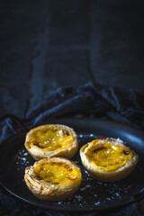Traditional portuguese dessert, pastel de nata, pasteis de nata, egg tart, on black background, vertical with copy space