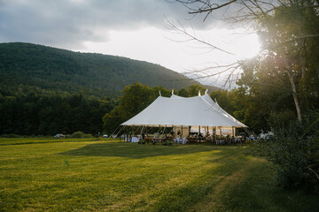sailcloth wedding tent in the middle of a field with sun shining through clouds behind it © Sophie