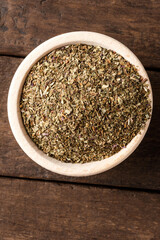 Dried basil leaves in bowl on wooden table. Close up. Top view