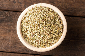 Dried rosemary leaves in bowl on wooden table. Close up. Top view