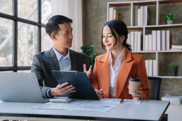 Business documents on office table with smart phone, tablet and laptop computer and graph with social network diagram and two colleagues discussing data in office.