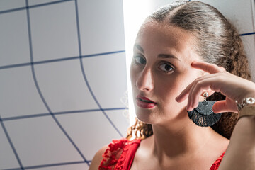 Portrait of a young woman with brown curly hair, black earrings, red dress and a backlit spotlight.