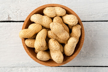 Overhead shot of peanuts in bowl on white wooden table. Healthy snacks