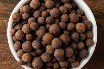 Allspice in bowl on rustic wooden table. Top view