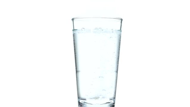 Fizzy tablet in glass of water isolated on white. Effervescent tablet dropped into the water