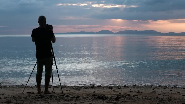Tripod shot of a photographer taking a sunset on a camera mounted on a tripod on the beach. Klong Muang Beach, Krabi Province, Thailand.