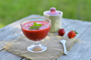 Strawberry smoothie in a glass decorated with mint leaves on rustic background, fresh fruit juice is red, detox food, diet and healthy breakfast, top view