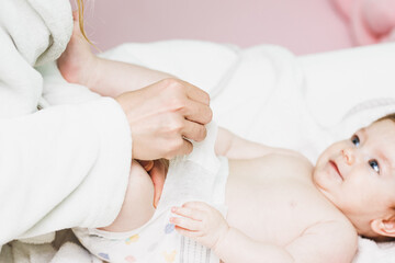 Mother putting diaper on baby in after bathing in bedroom