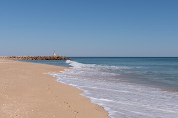 Beach and lighthouse on jetty on Tavira Island, known as Ilha de Tavira in the Algarve in Portugal.