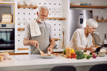 a happy senior couple preparing a healthy meal together, using a tablet